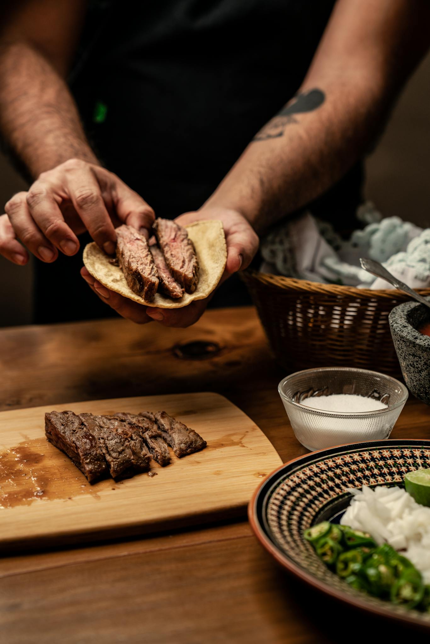 Close-up of hands preparing a steak taco with fresh ingredients on a wooden board.