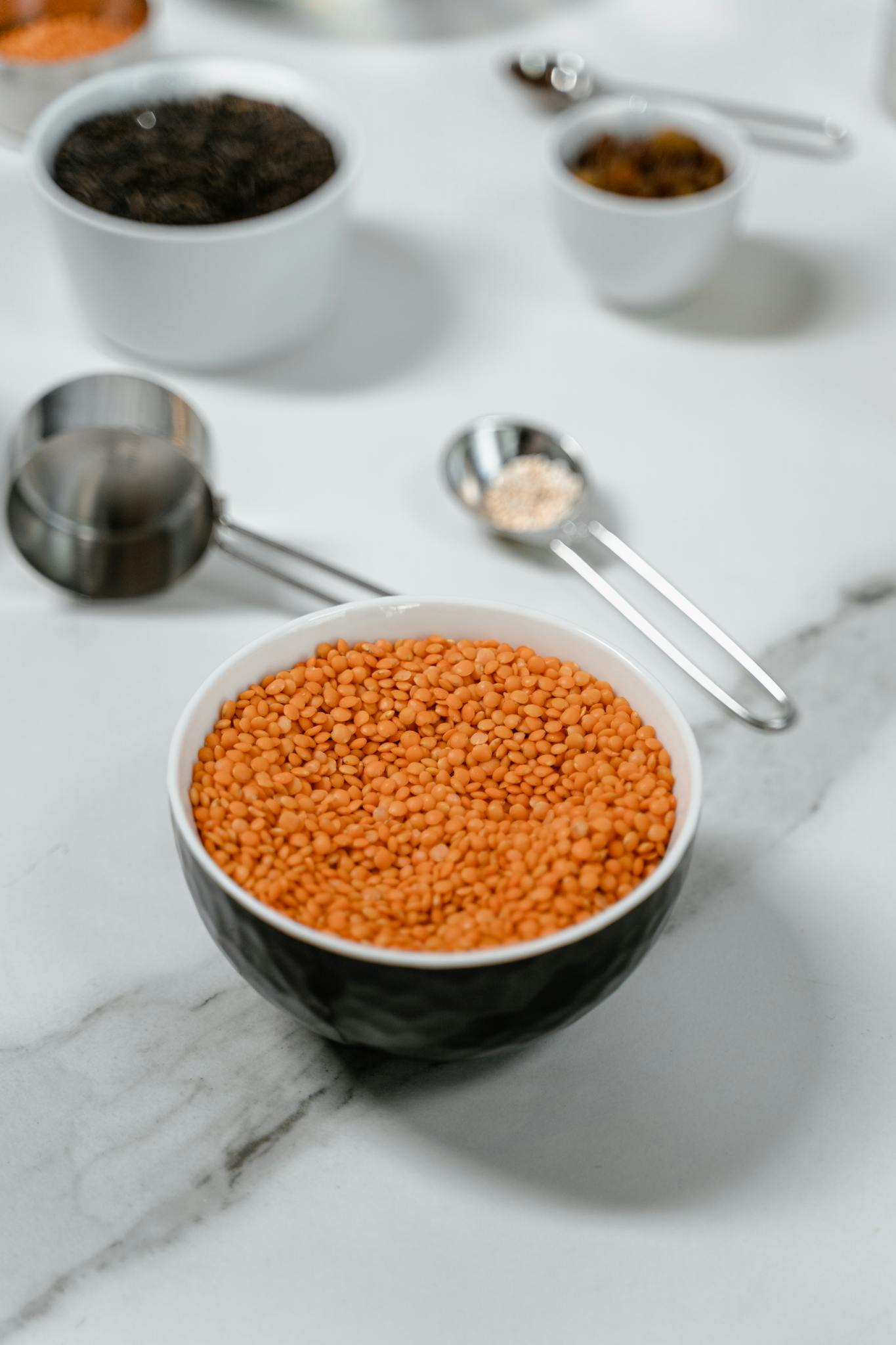 Red lentils in a bowl on marble, surrounded by measuring spoons.